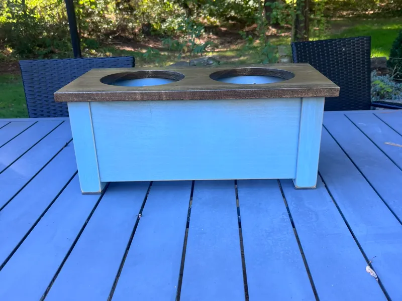 Low blue dog bowl stand with a brown stained top and two bowls, photographed on an outdoor patio table