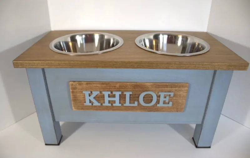 Blue painted dog bowl stand with a brown stained top, two stainless steel bowls and a matching nameplate reading Khloe in blue letters